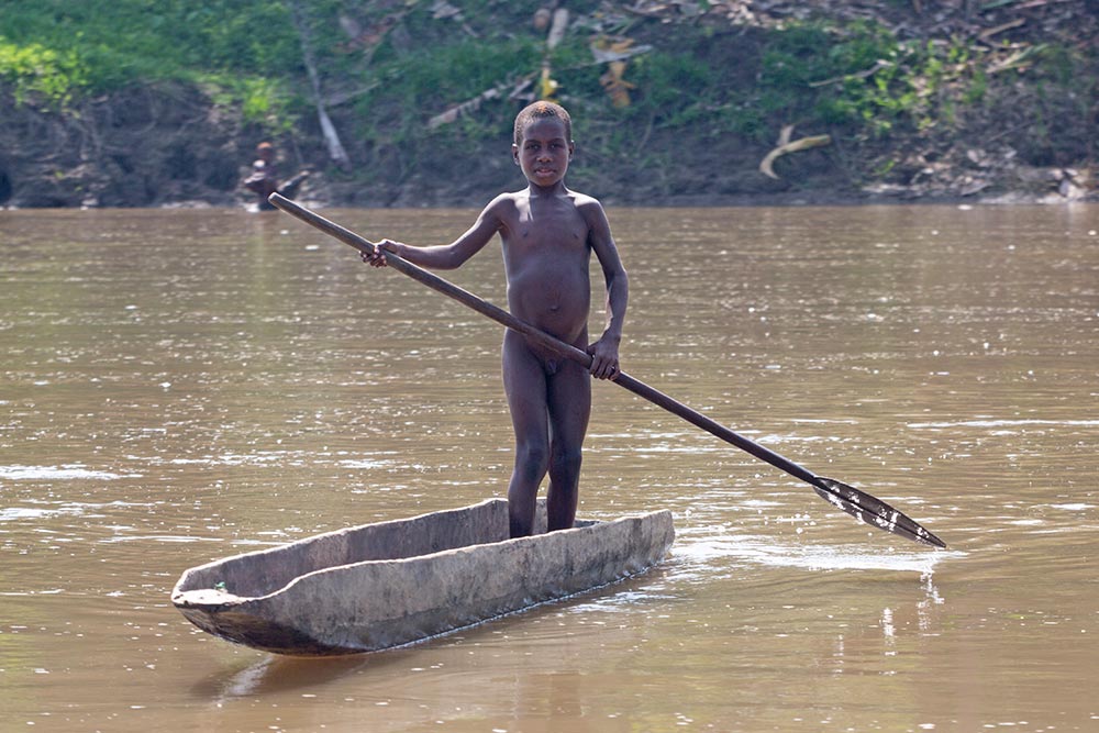 A young boy paddling in a dugout canoe in the Karawari river.